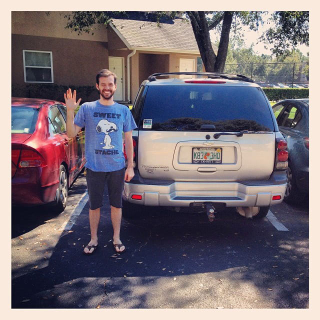 Tanner standing next to his car, waving goodbye to the camera.