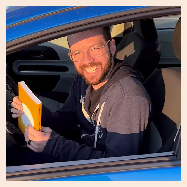 Tanner sitting in his car, holding a book and smiling at the camera.